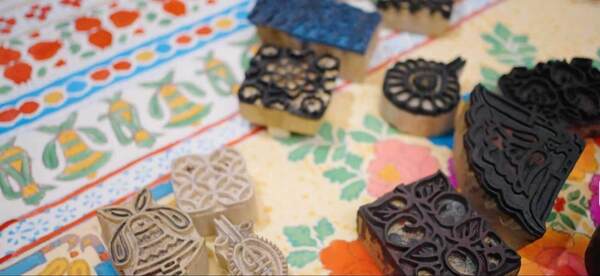 A collection of varied wooden and rubber block printing stamps on two distinct colorful fabrics with floral and bell designs.