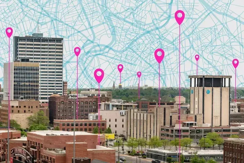 Bright pink pins descend from a map-patterned sky onto the South Bend cityscape.