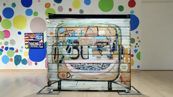 Colorful graffiti art of a smiling face on a corrugated panel with a polka-dot wall behind.